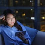 Woman watching videos on mobile device while sitting on sofa at night