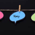 Three languages on speech bubbles hanging on the rope, black background, with the words Ahí, Hay, and Ay