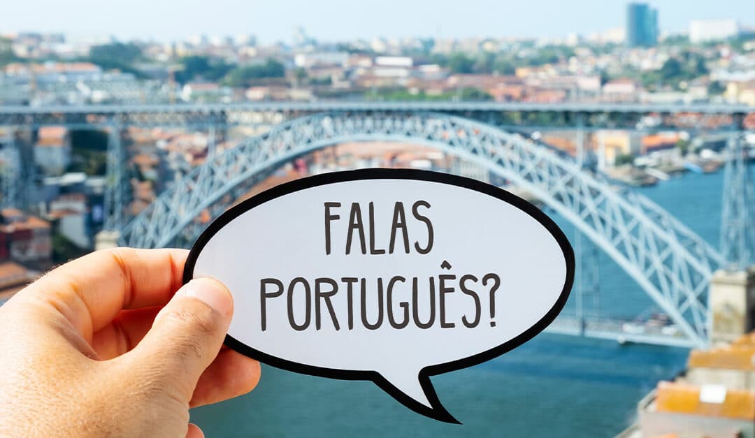 the hand of a man holding a speech bubble with the question falas portugues, do you speak Portuguese? written in Portuguese, in Porto, Portugal, with the famous Dom Luis I Bridge in the background