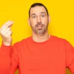 Bearded man in his 40s wearing a red jumper making the Italian mamma mia gesture isolated on yellow studio background.