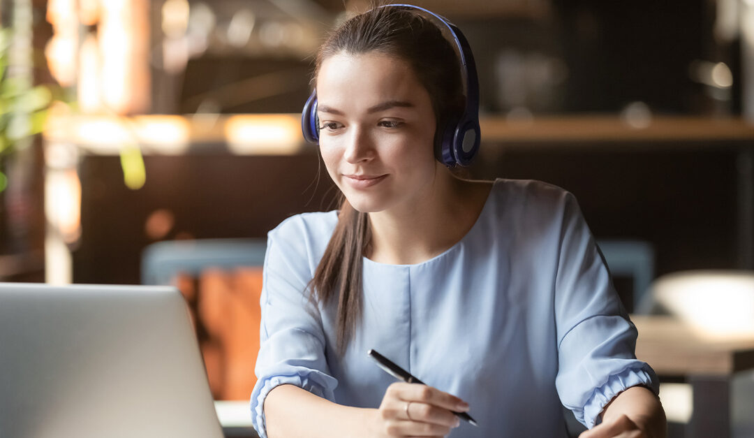 Focused woman wearing headphones using laptop in cafe, learning Portuguese on YouTube