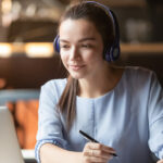 Focused woman wearing headphones using laptop in cafe, learning Portuguese on YouTube