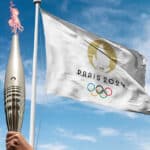 Paris, France 2024 Olympics flag waving at cloudy sky background. with the olympics flame holding by athlete.