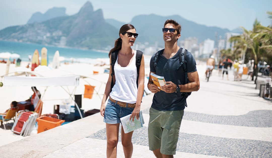 Young tourist couple walking on beach in Brazil with a map and cultural tips guidebook on holiday in summer