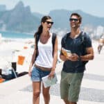 Young tourist couple walking on beach in Brazil with a map and cultural tips guidebook on holiday in summer