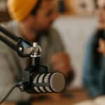 Two cheerful Portuguese people recording a podcast in a studio. Focus on the microphone in the foreground.