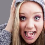 Blonde woman in hooded shirt with her hands on the side of her head and her tongue twisted and slightly out