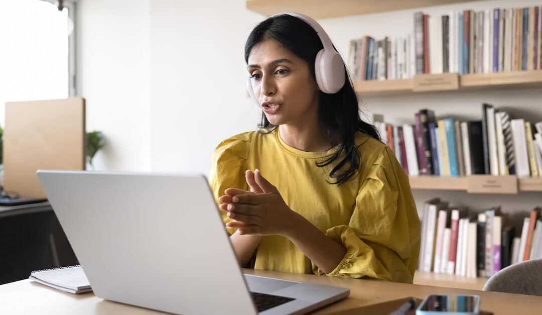 Young woman with headphones speaking to an online language tutor on her laptop