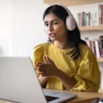Young woman with headphones speaking to an online language tutor on her laptop
