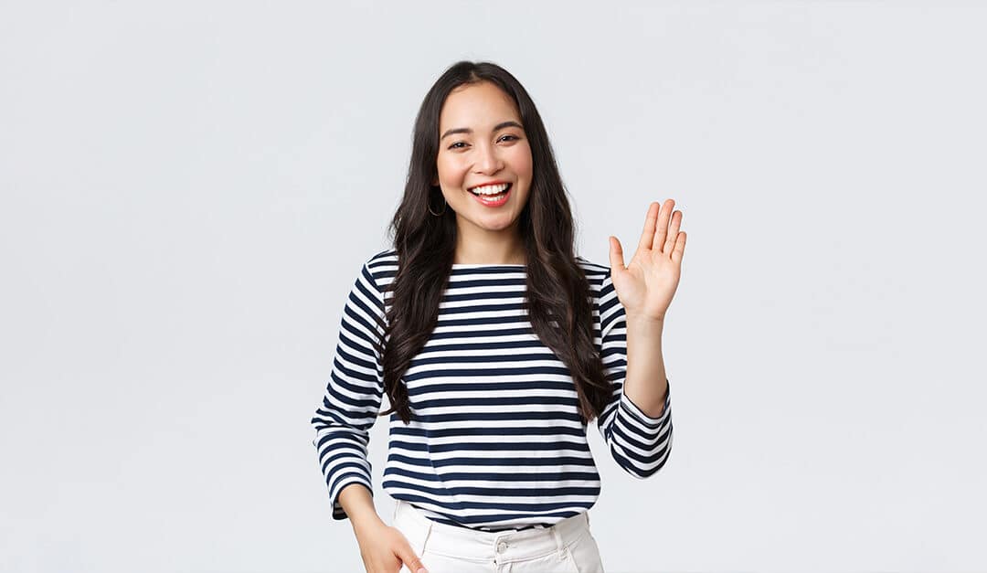 Woman against a white background smiling and waving hello to the camera
