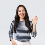 Woman against a white background smiling and waving hello to the camera