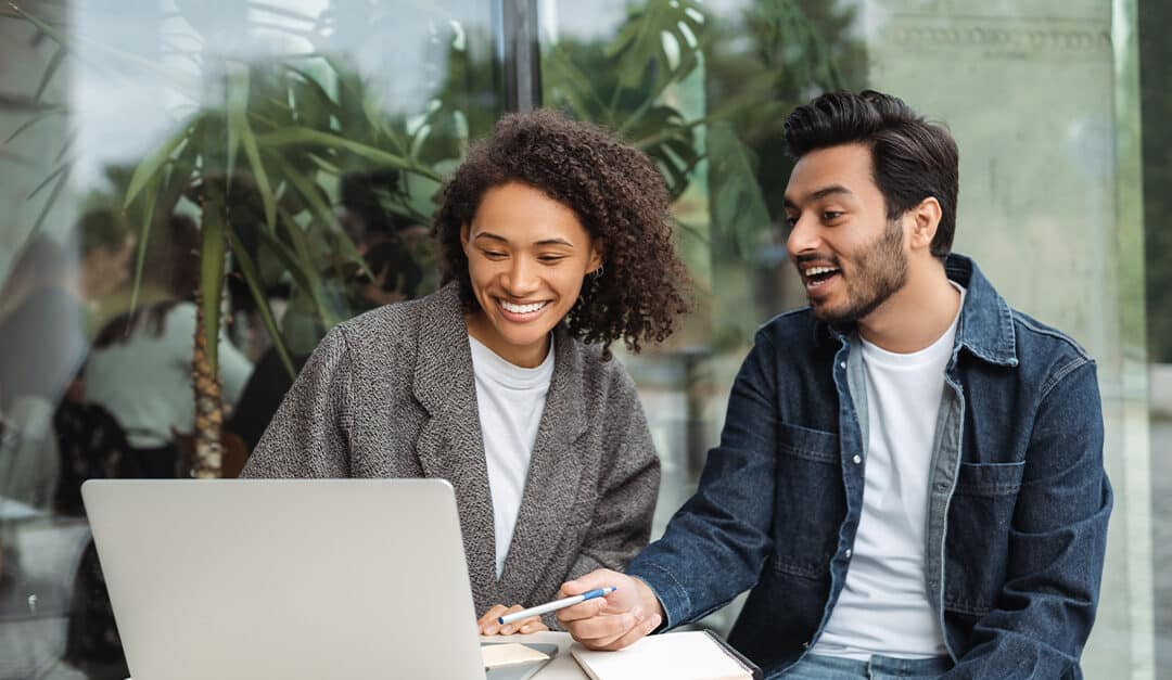 Young adult woman and man sitting outside looking at a laptop together and laughing