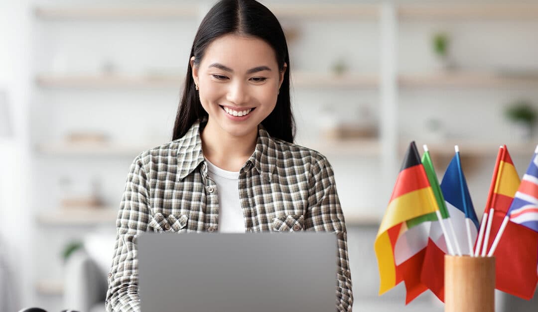 Young woman in a bright modern home office on a laptop with a cup next to her on the desk with multiple flags of various nationalities