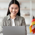 Young woman in a bright modern home office on a laptop with a cup next to her on the desk with multiple flags of various nationalities